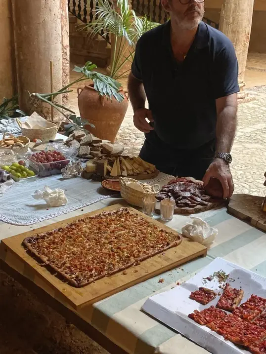 Personas preparando y compartiendo platos locales en una mesa larga dentro de un patio mediterráneo histórico, capturando una experiencia gastronómica auténtica en las Islas Baleares.