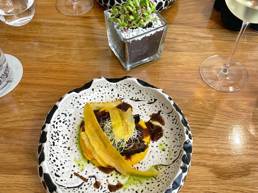 Plated dish at Restaurant Xalest in Palma, served on a stylish ceramic plate with wine glasses on the table.