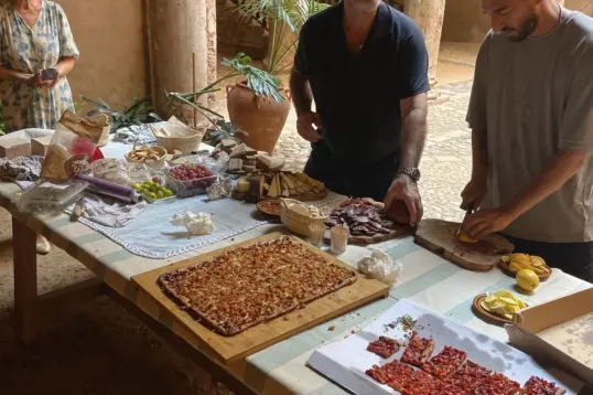 People preparing and sharing local dishes on a long table in a historic Mediterranean courtyard, capturing an authentic food experience in the Balearic Islands.