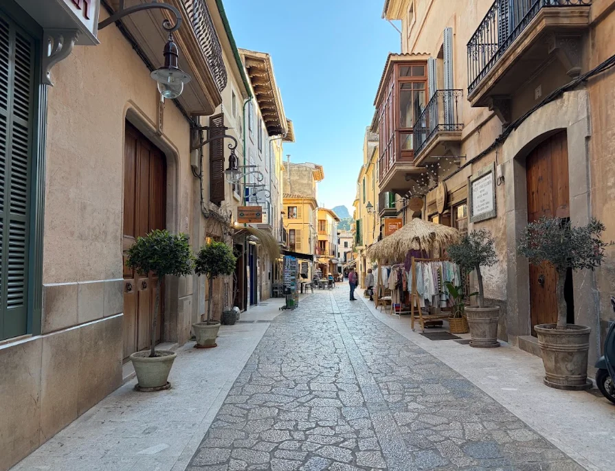 Traditional stone street in Pollença old town with boutique shops and mountain views in northern Mallorca.