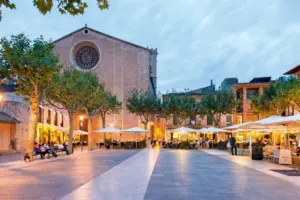 Plaça Major in Pollença at sunset with restaurant terraces and the Church of Our Lady of the Angels in Mallorca