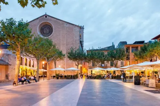 Plaça Major in Pollença at sunset with restaurant terraces and the Church of Our Lady of the Angels in Mallorca