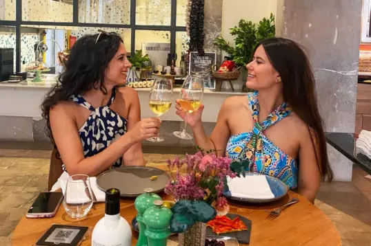 Two women toasting with glasses of white wine during a local dining experience at a restaurant in Palma de Mallorca