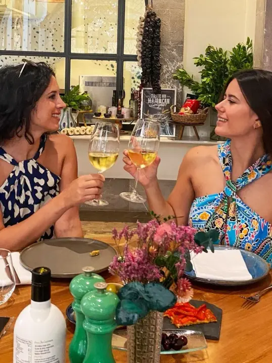 Two women toasting with glasses of white wine during a local dining experience at a restaurant in Palma de Mallorca