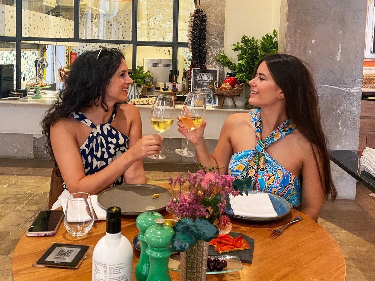Two women toasting with glasses of white wine during a local dining experience at a restaurant in Palma de Mallorca